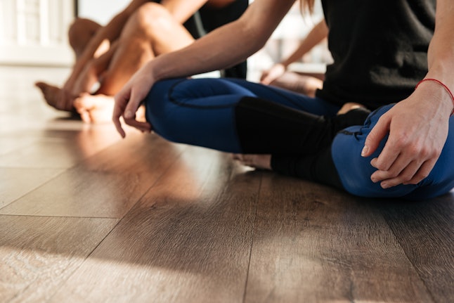 Closeup of woman sitting with legs crossed and practicing yoga in group at studio