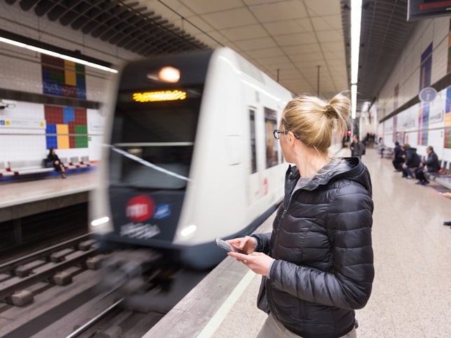 Jeune femme occasionnelle avec un téléphone portable à la main qui attend le métro sur le quai d'une station de métro. Transport public.